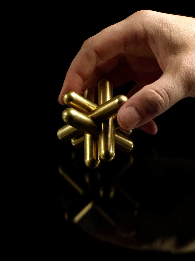 Hand holding the brass Craighill Jack Puzzle on Black background