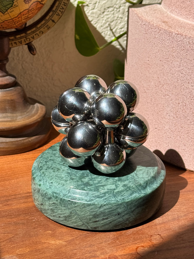 The silver Curio Atom Puzzle assembled on the Rajasthan Green marble Curio Plinth, lifestyle desk shot with globe