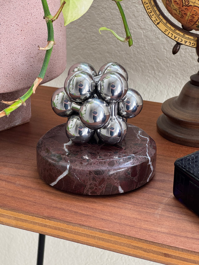 The silver Curio Atom Puzzle assembled on the Roso Lepanto marble Curio Plinth, lifestyle desk shot with globe