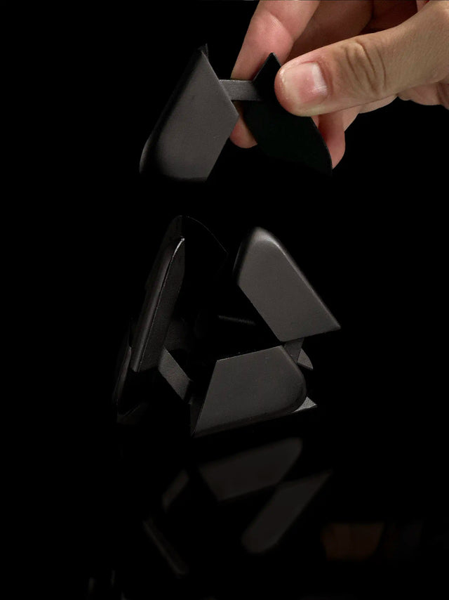 A hand reaches to assemble the black Curio Tetra Puzzle against a black background