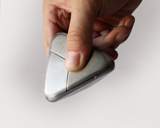 A hand assembling the stainless steel Craighill Tetra Puzzle on a gray background