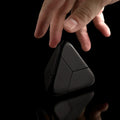 A hand reaches for a black Criaghill Tetra Puzzle on a black background. 