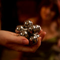 The assembled silver Curio Atom Puzzle resting in an open palm, lifestyle shot with warm dark background