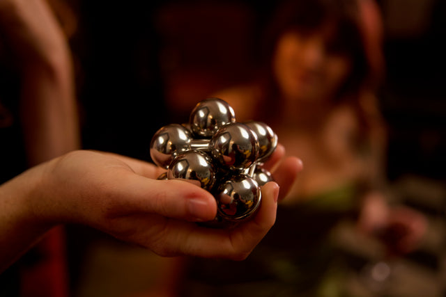 The assembled silver Curio Atom Puzzle resting in an open palm, lifestyle shot with warm dark background