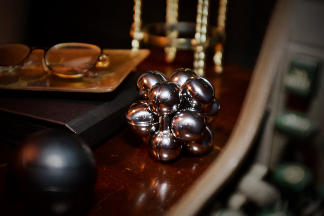 The assembled silver Curio Atom Puzzle resting on a dark wood desk surrounded by objects, lifestyle shot