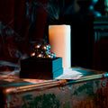 The assembled silver Curio Atom Puzzle resting on its gift box, styled with playing cards, a lit candle, and a vintage trunk, lifestyle shot