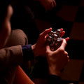 Two hands manipulating the assembled silver Curio Atom Puzzle, lifestyle shot with dark moody background