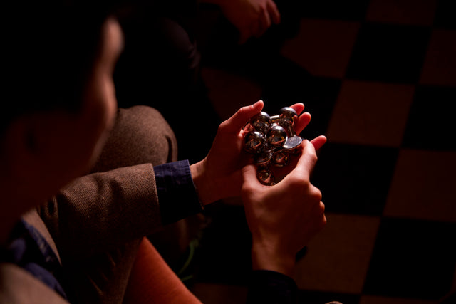 Two hands manipulating the assembled silver Curio Atom Puzzle, lifestyle shot with dark moody background