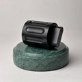 A black Curio Column Puzzle resting on its side on top of a green marble Curio Plinth on a white background