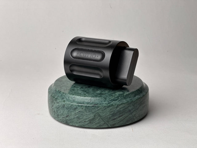 A black Curio Column Puzzle resting on its side on top of a green marble Curio Plinth on a white background