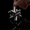 A hand pulling one bar from the assembled stainless steel Curio Jack Puzzle on a black reflective surface