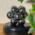 The silver Curio Atom Puzzle assembled on a dark marble Curio Plinth, lifestyle shelf shot with ivy plant
