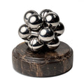 A silver Curio Atom Puzzle resting on a Dark Emperador Curio Plinth on a white background