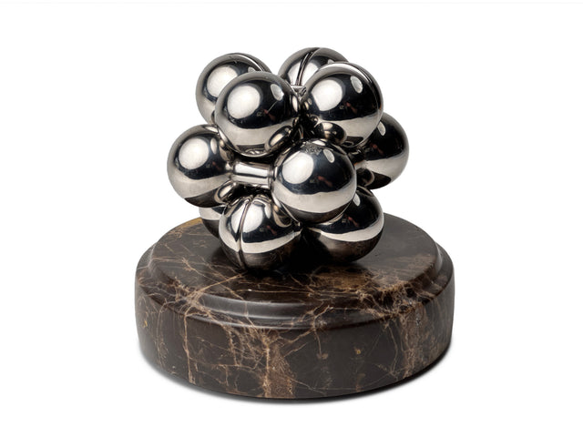 A silver Curio Atom Puzzle resting on a Dark Emperador Curio Plinth on a white background