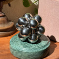 The silver Curio Atom Puzzle assembled on the Rajasthan Green marble Curio Plinth, lifestyle desk shot with globe