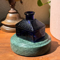 A decorative cobalt glass figurine displayed on the Rajasthan Green marble Curio Plinth, lifestyle desk shot showing display versatility