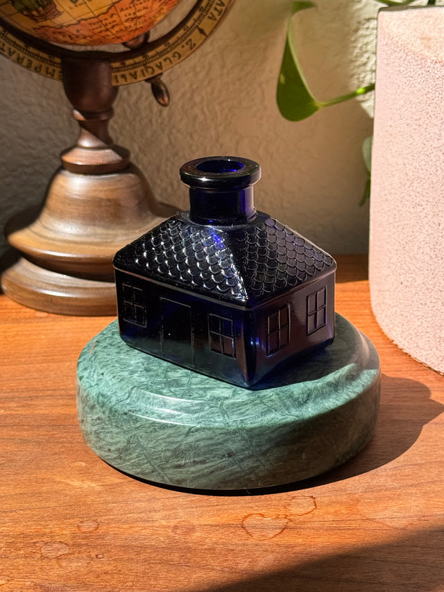 A decorative cobalt glass figurine displayed on the Rajasthan Green marble Curio Plinth, lifestyle desk shot showing display versatility