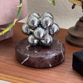 The silver Curio Atom Puzzle assembled on the Roso Lepanto marble Curio Plinth, lifestyle desk shot with globe