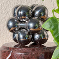 The silver Curio Atom Puzzle assembled on the Roso Lepanto marble Curio Plinth, lifestyle shelf shot with ivy