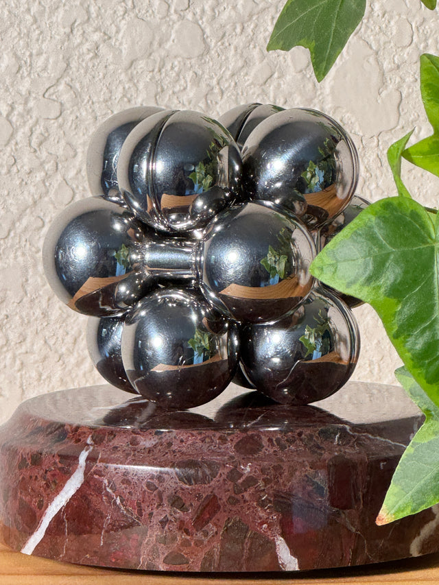The silver Curio Atom Puzzle assembled on the Roso Lepanto marble Curio Plinth, lifestyle shelf shot with ivy