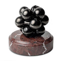 A black Curio Atom Puzzle resting on a Roso Lepanto Curio Plinth on a white background