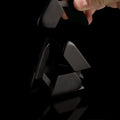 A hand reaches to assemble the black Curio Tetra Puzzle against a black background