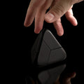A hand reaches for the black Curio Tetra Puzzle on a black background
