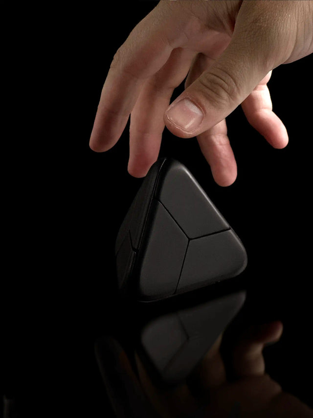 A hand reaches for the black Curio Tetra Puzzle on a black background