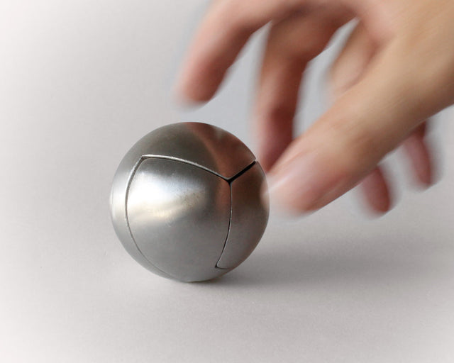 A hand holding the stainless steel Craighill Venn Puzzle on a gray background